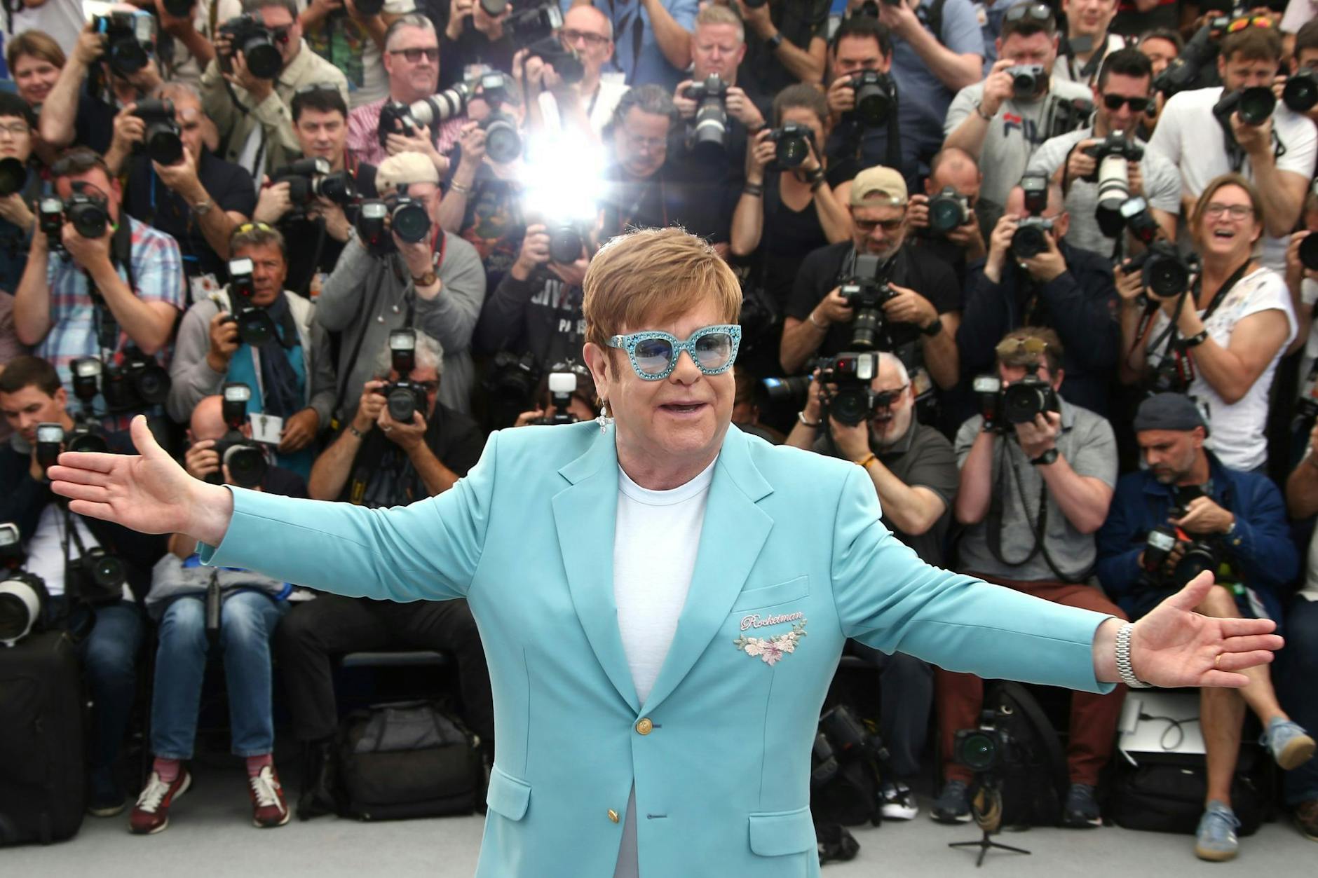 Elton John umgeben von Fotografen.