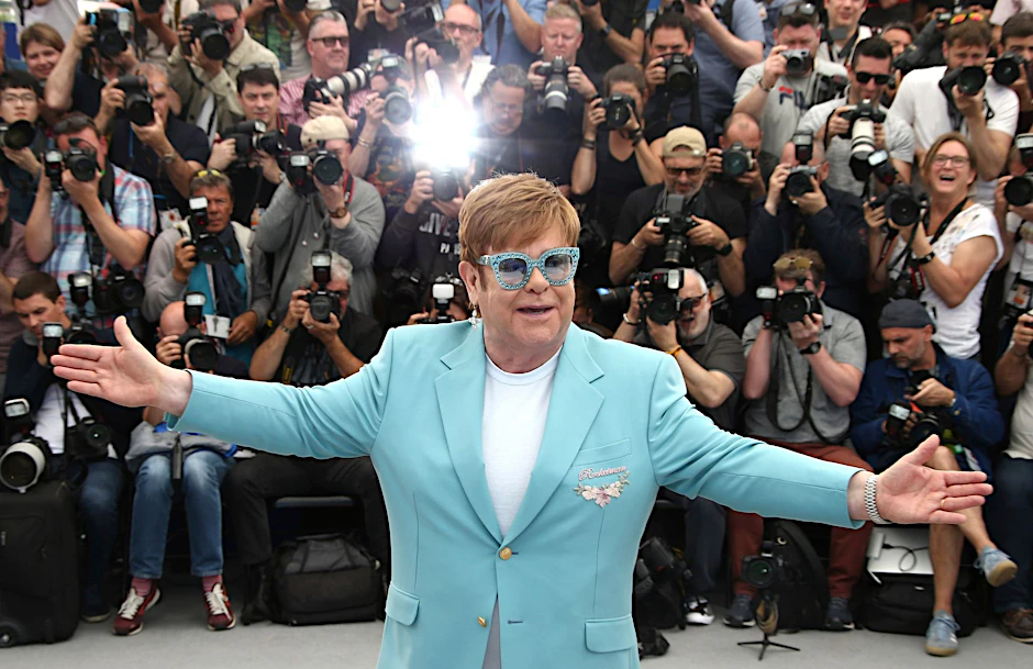 Elton John umgeben von Fotografen.