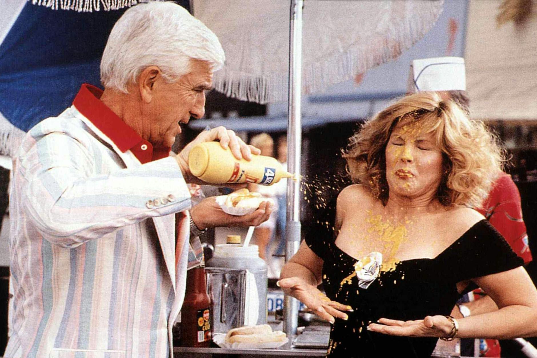 Leslie Nielsen gibt in „Die nackte Kanone“ seinen Senf dazu. Dabei gehört das goldene Glück auf den Hotdog und nicht aufs Dekolleté von Priscilla Presley.