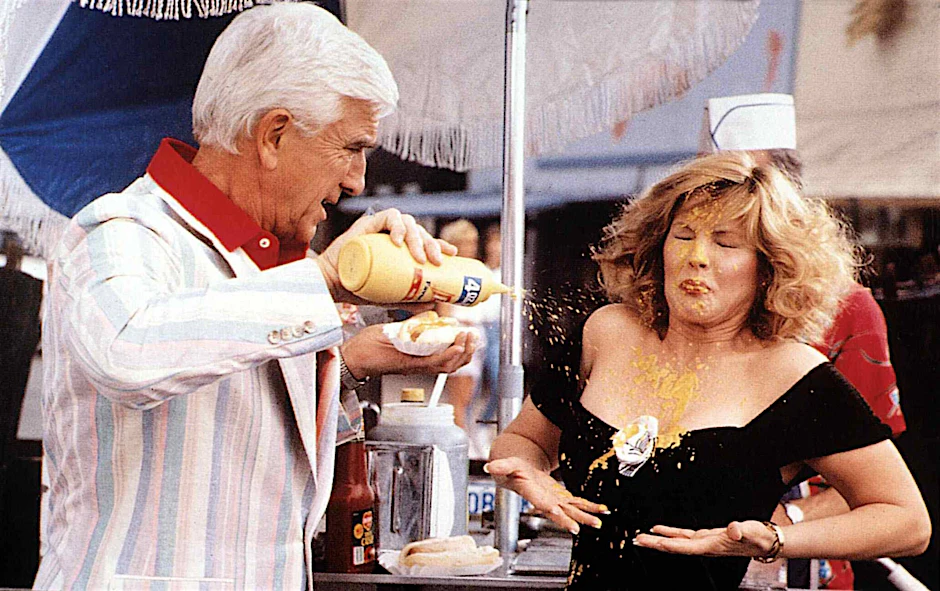 Leslie Nielsen gibt in „Die nackte Kanone“ seinen Senf dazu. Dabei gehört das goldene Glück auf den Hotdog und nicht aufs Dekolleté von Priscilla Presley.
