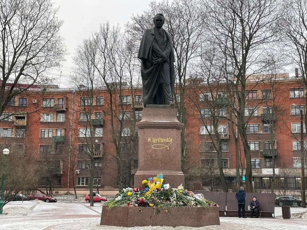 Blumen am Fuß des Taras Schewtschenko-Denkmals in St. Petersburg, teilweise in blaues und gelbes Papier gehüllt – die Farben der Ukraine.