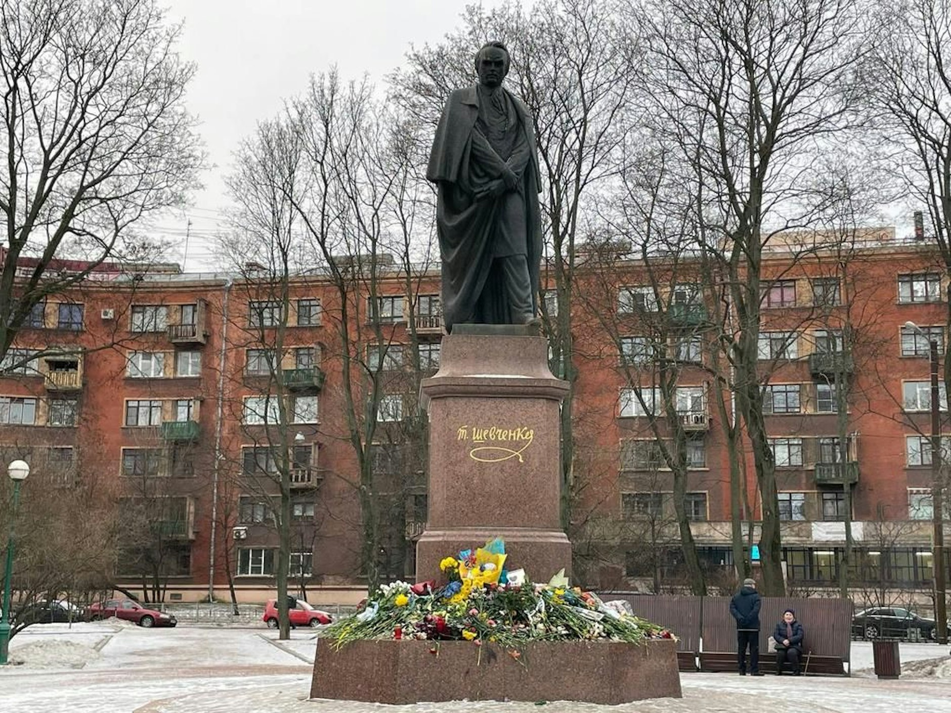 Blumen am Fuß des Taras Schewtschenko-Denkmals in St. Petersburg, teilweise in blaues und gelbes Papier gehüllt – die Farben der Ukraine.