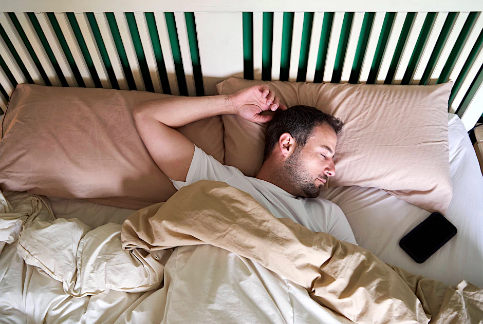 Mann schläft mit Handy im Bett.