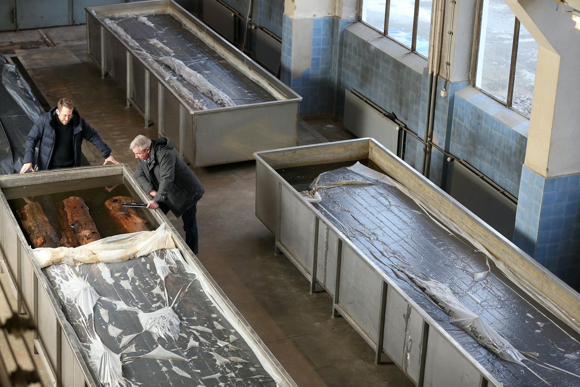 Die gesicherten Stämme des Bohlenweges vom Molkenmarkt, der ältesten Straße Berlins, werden in einem Bad konserviert. Landesarchäologe Matthias Wemhoff (r.) und Chefrestaurator Philipp Schmidt-Reimann (l.) überwachen den Prozess.