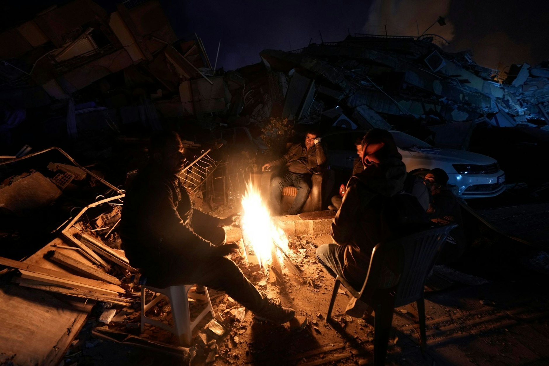 Menschen wärmen sich an einem Feuer vor Gebäuden, die bei den Erdbeben in der Türkei zerstört wurden.