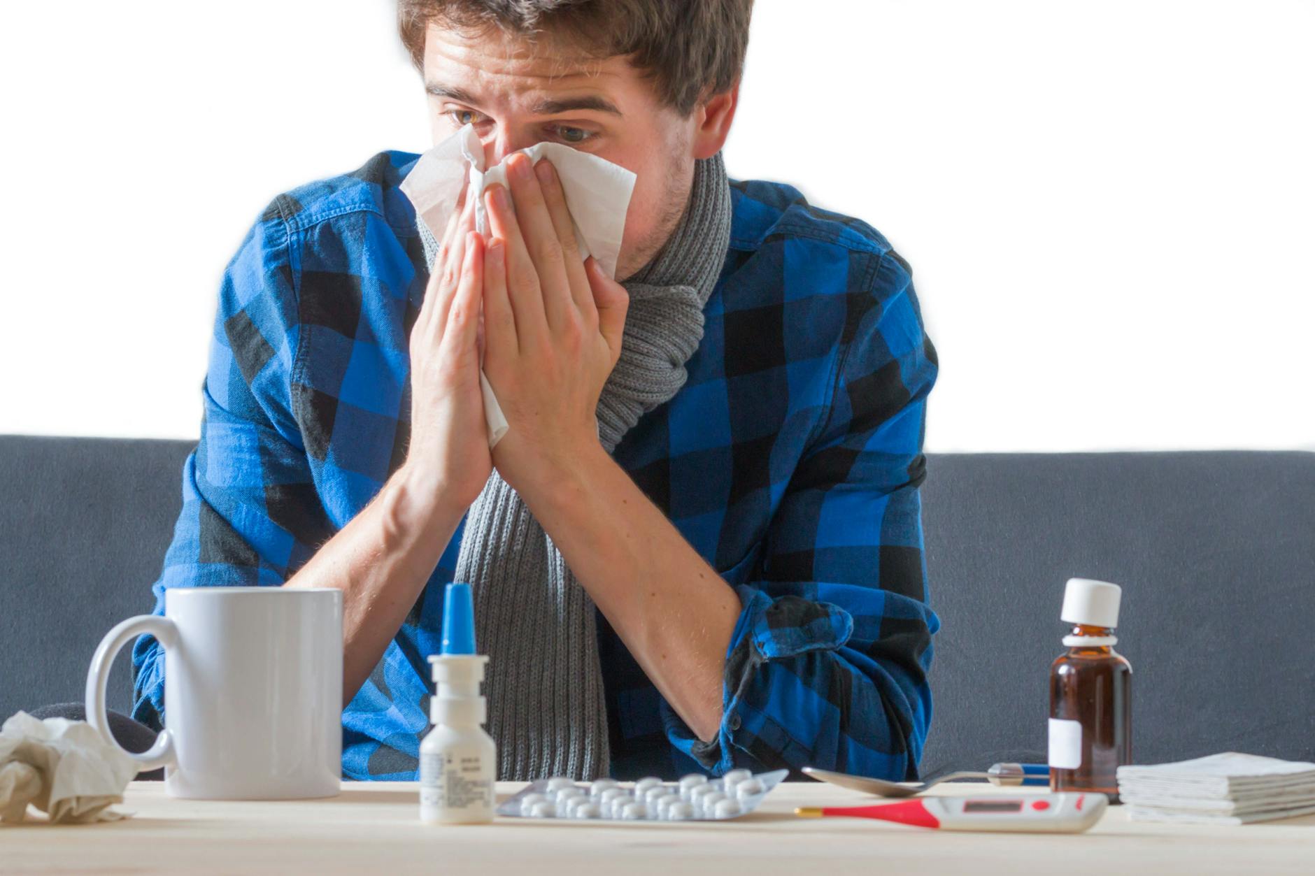 Mann sitzt auf Sofa und putzt sich die Nase.