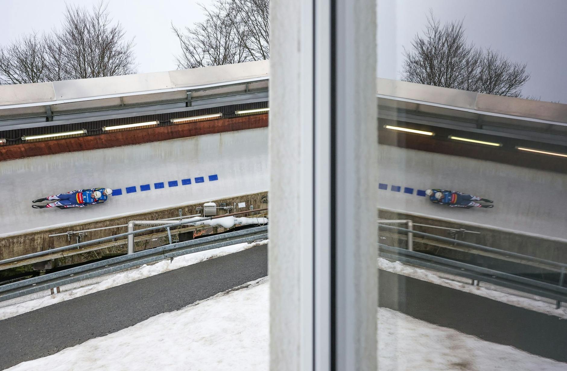 Doppelt gedoppelt: Thomas Steu (l) und Lorenz Koller aus Österreich fahren durch den Eiskanal und spiegeln sich dabei in der Scheibe eines Gebäudes.