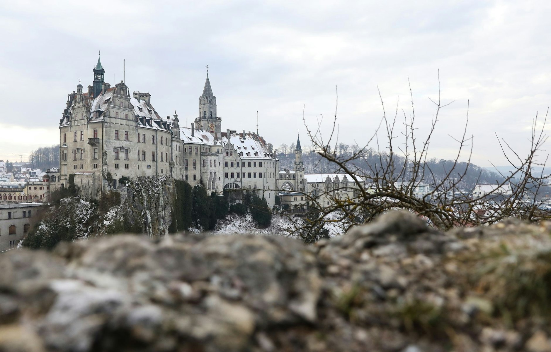 Hinter einem Felsen ragt das leicht mit Schnee bedeckte Schloss Sigmaringen, auch Hohenzollernschloss genannt, hervor.  