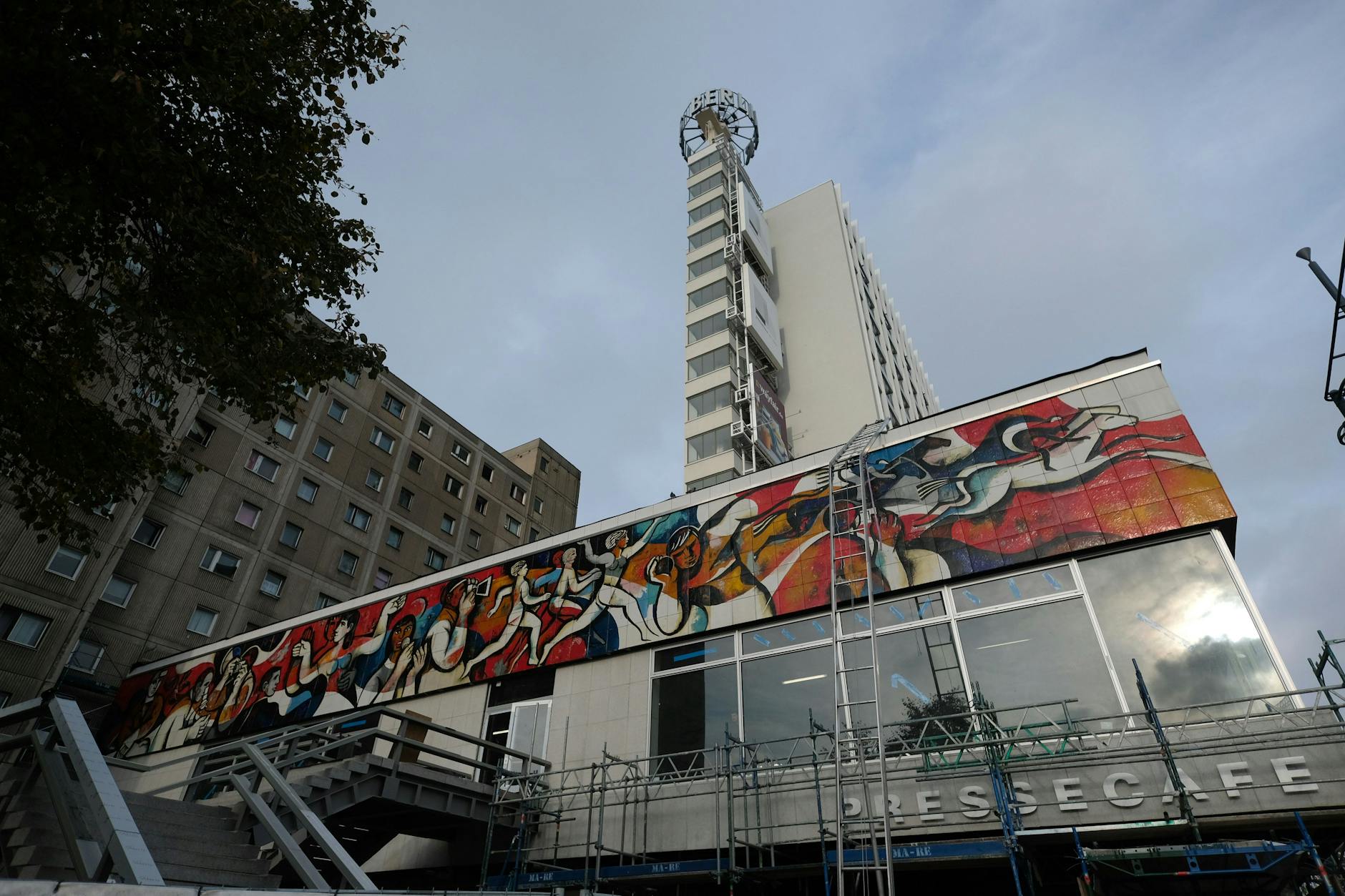 Sozialistische Kunst am Bau: Das Fries am einstigen Pressecafé wurde nach der Sanierung 2021 wieder sichtbar. Dem Motto „Die Presse als Organisator“ gemäß wird gezeigt, was zu organisieren sei: Sport, Vergnügen, Bildung.