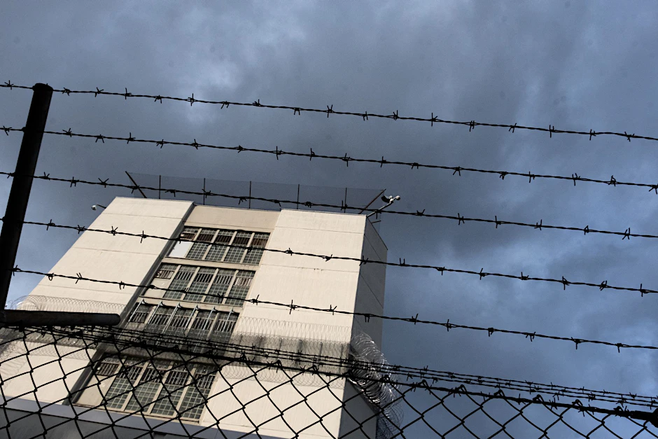 Ein Stacheldrahtzaun umzäunt das Gelände einer Justizvollzugsanstalt.  