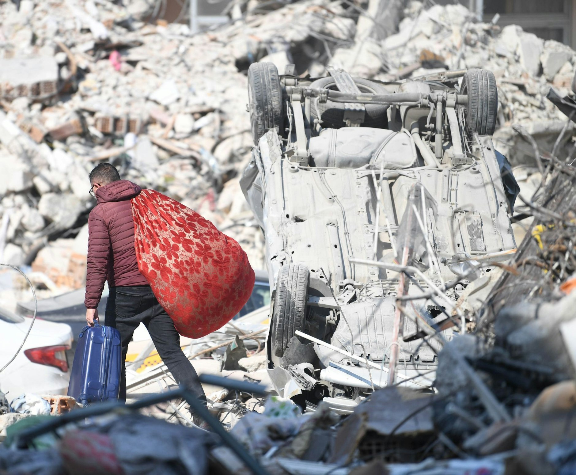 Ein Mann läuft mit seinen Habseligkeiten über Erdbebentrümmer in Antakya.  