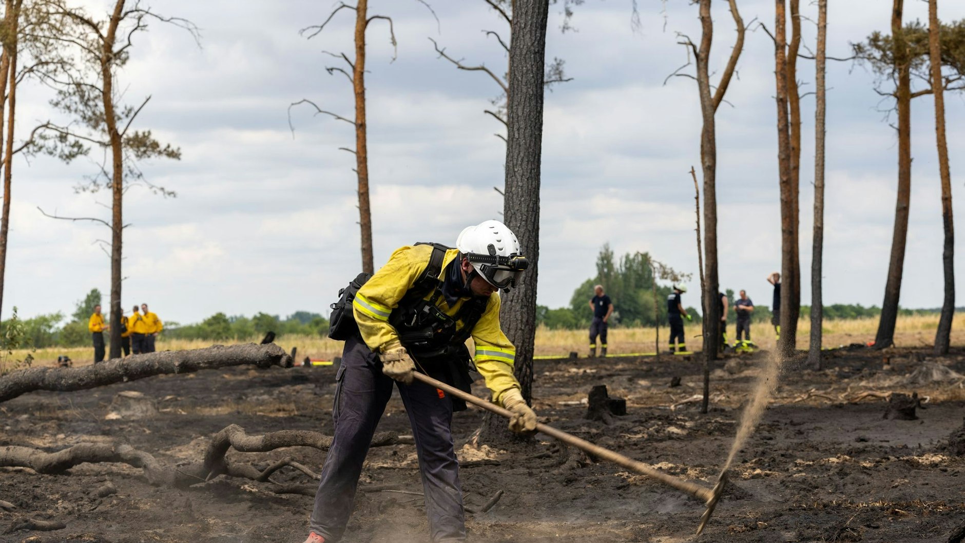 Ein Feuerwehrmann bearbeitet nach einem Waldbrand den Waldboden mit einer Hacke.