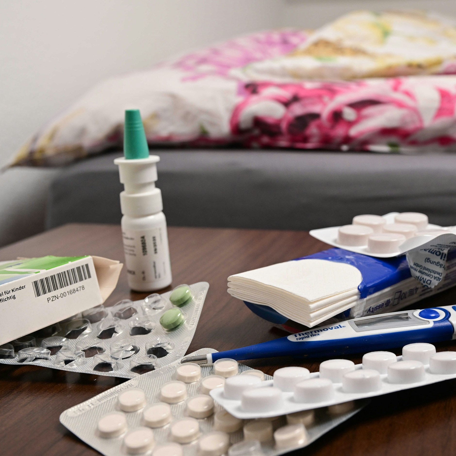 Ein Fieberthermometer und Medikamente liegen auf einem Nachttisch.
