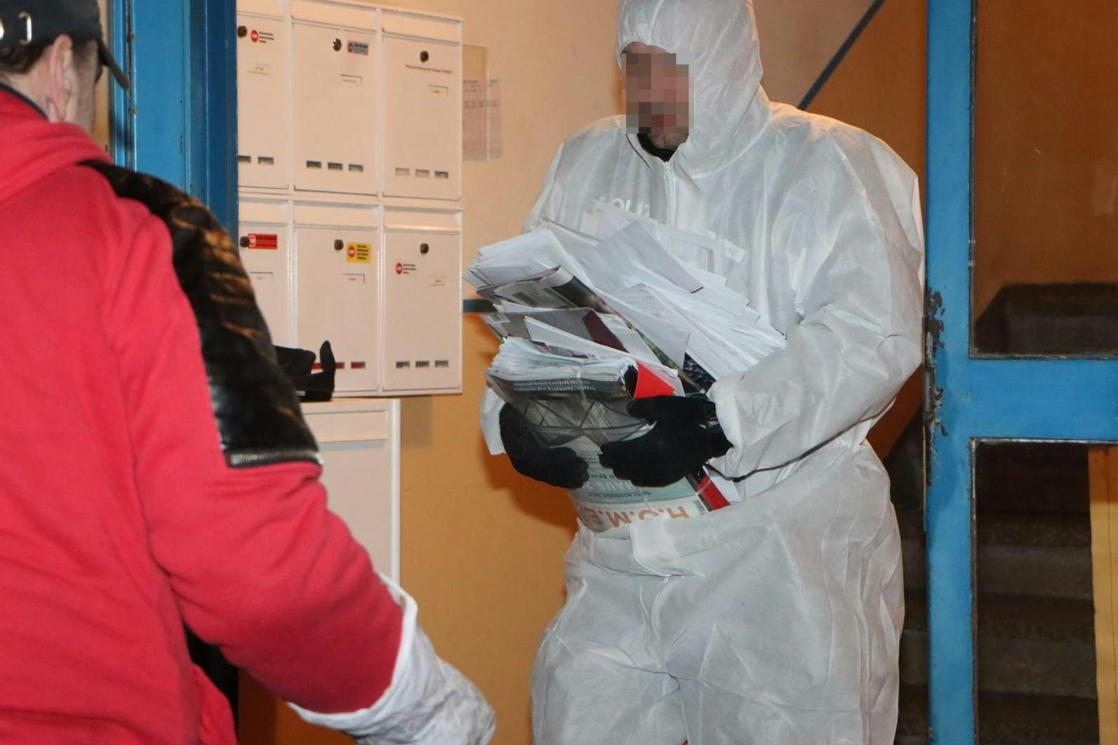 Ein Mann im Schutzanzug trägt unterschlagene Post aus der Wohnung der Zustellerin.