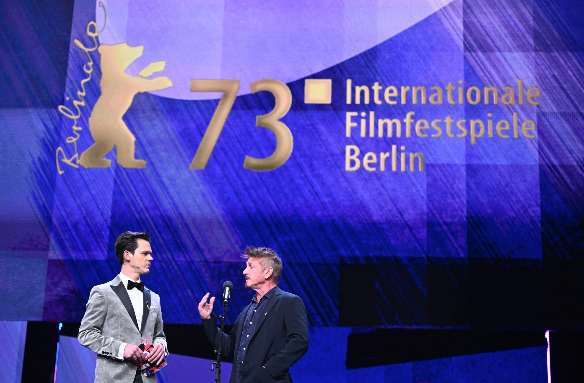 Jo Schück, Moderator der Berlinale Eröffnungsveranstaltung und der Schauspieler und Filmregisseur Sean Penn unterhalten sich auf der Bühne bei der Eröffnung der Berlinale.  