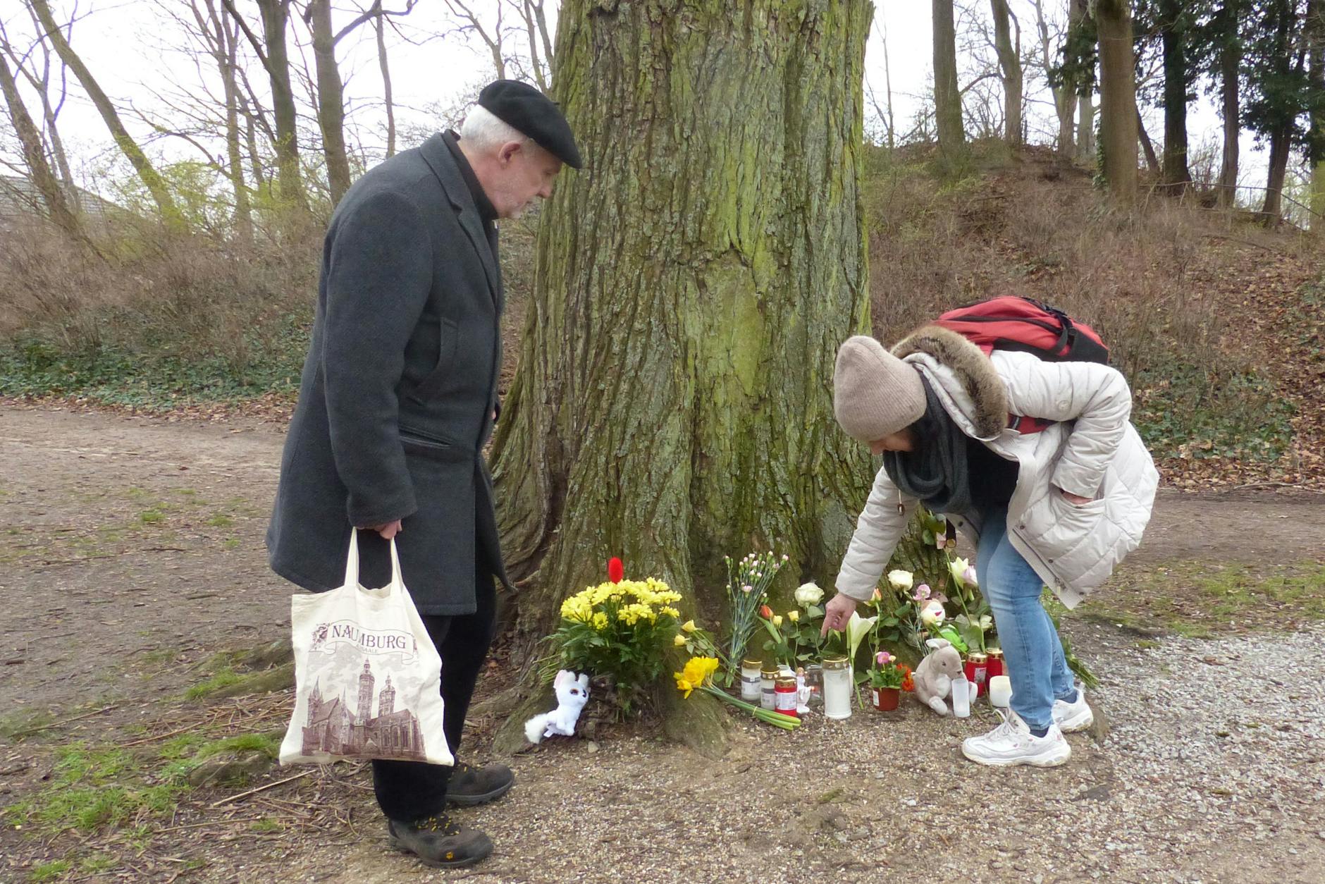 Im Park gibt es einen zweiten Ort, an dem Menschen Blumen ablegen, am Fuß eines Baums.