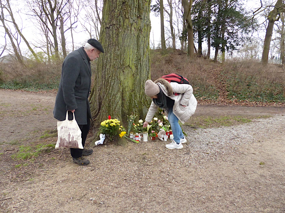 Im Park gibt es einen zweiten Ort, an dem Menschen Blumen ablegen, am Fuß eines Baums.