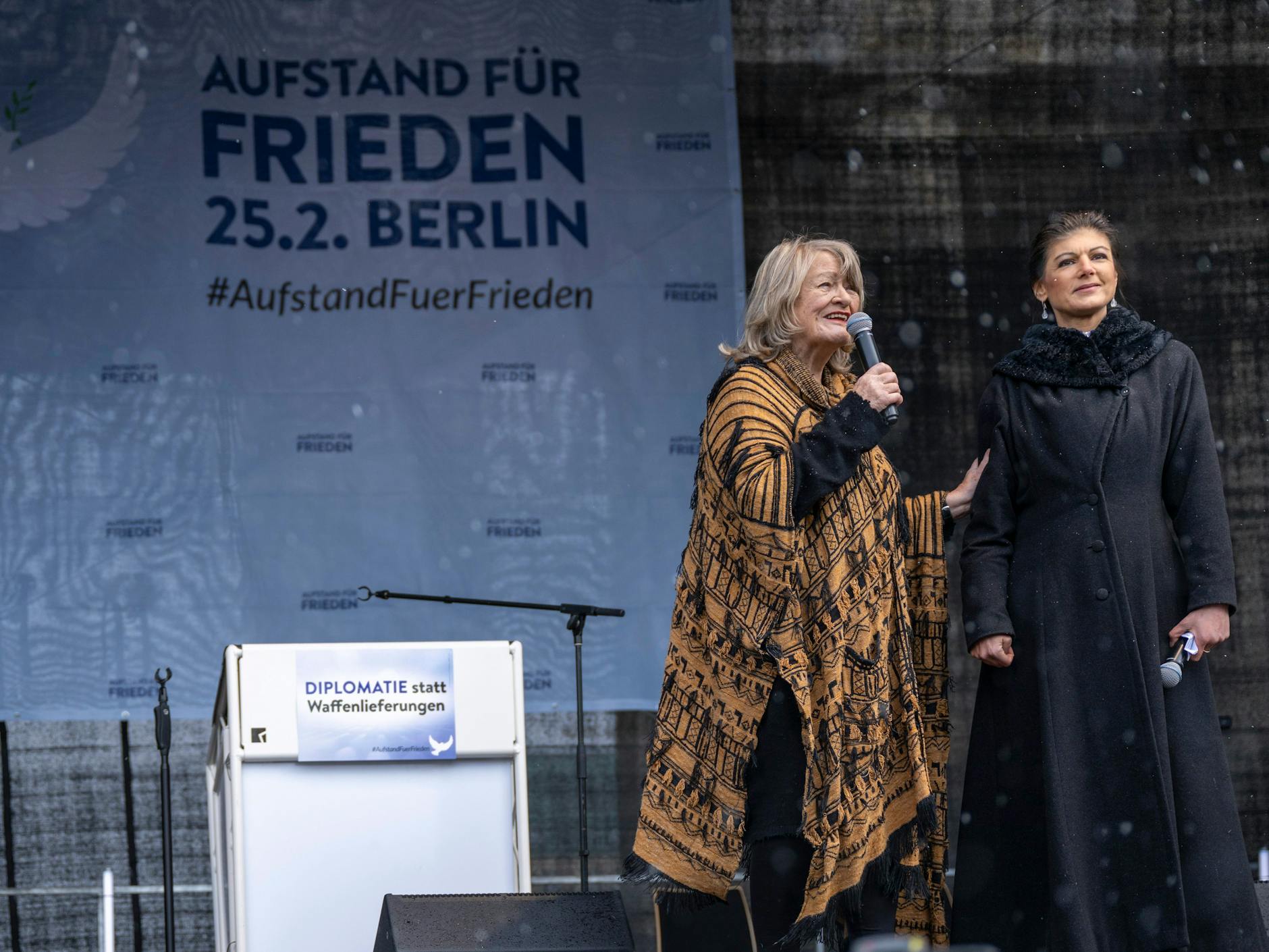 Alice Schwarzer (l.) und Sahra Wagenknecht begrüßen die zahlreichen Teilnehmer vor dem Brandenburger Tor, die trotz Schneeregens gekommen sind.