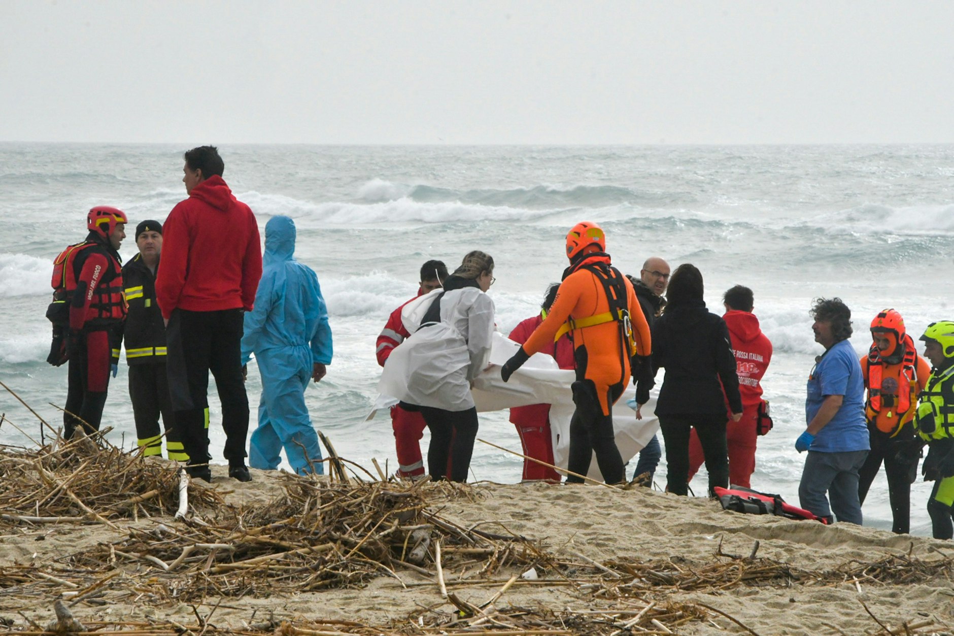 Helfer bergen einen Leichnam an der Küste Kalabriens. Das Mittelmeer ist aufgewühlt.