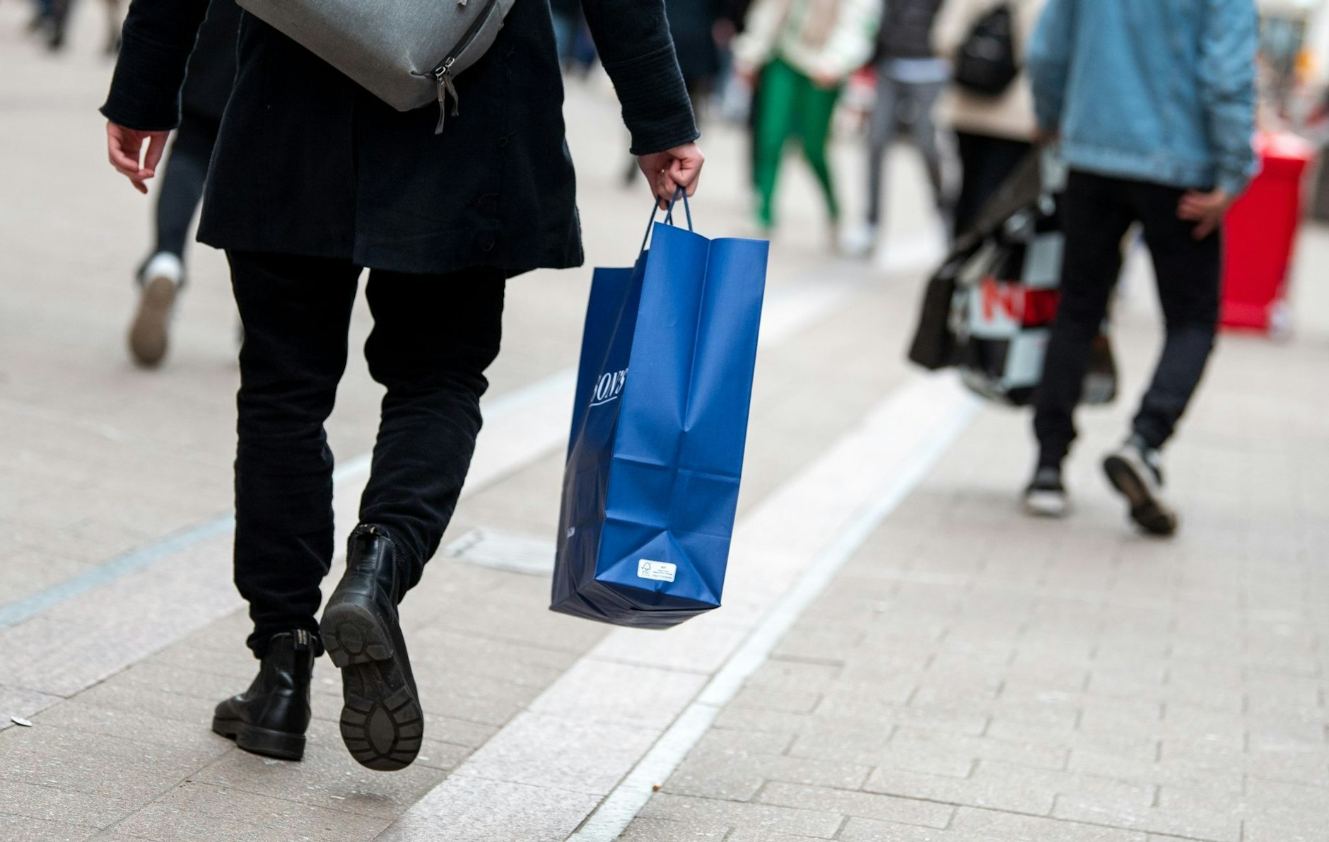 Ein Passant mit Einkaufstüten geht in der Innenstadt durch eine Einkaufsstraße.  