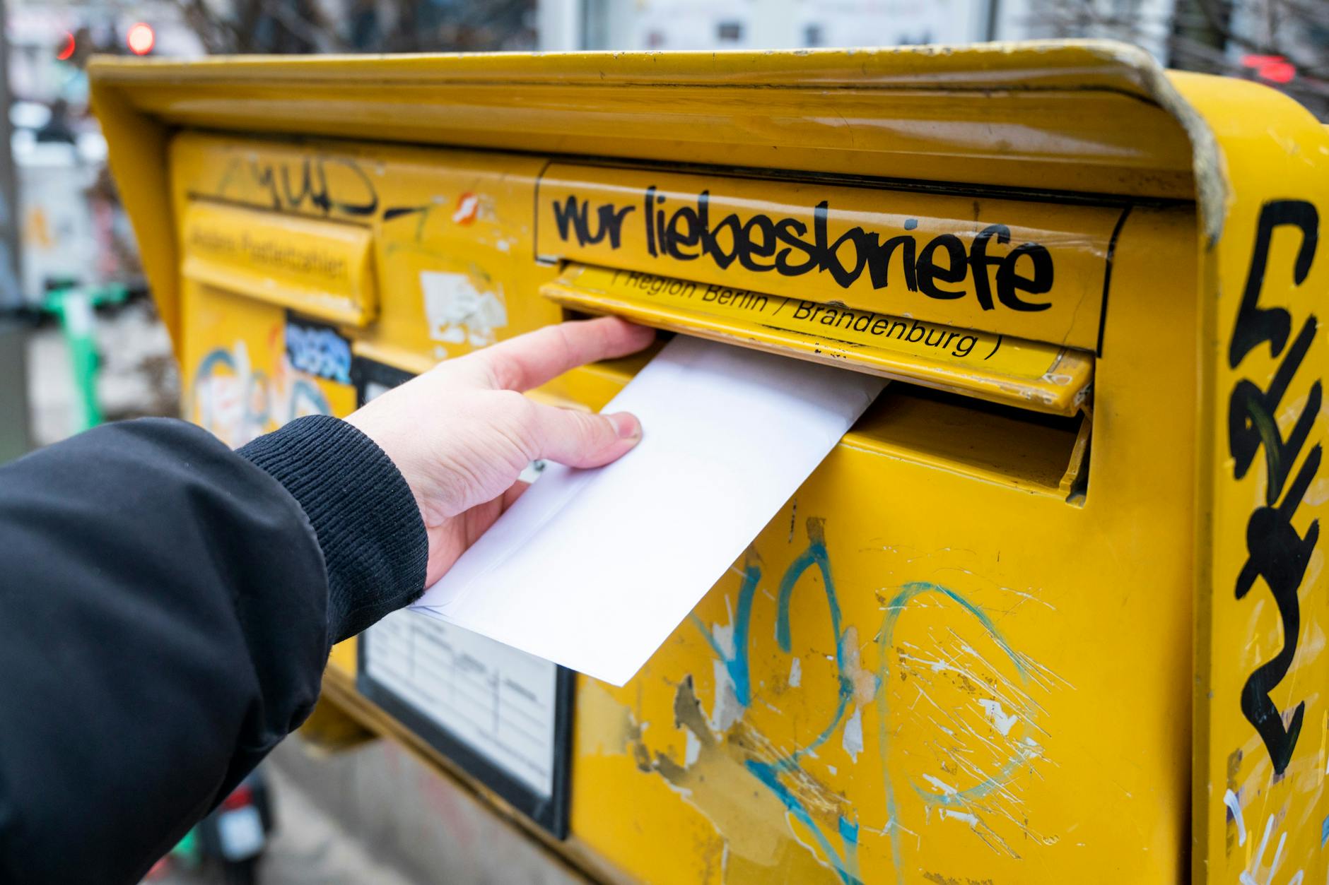 Ein Mann wirft einen Brief in einen Briefkasten.