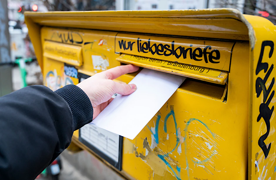Ein Mann wirft einen Brief in einen Briefkasten.
