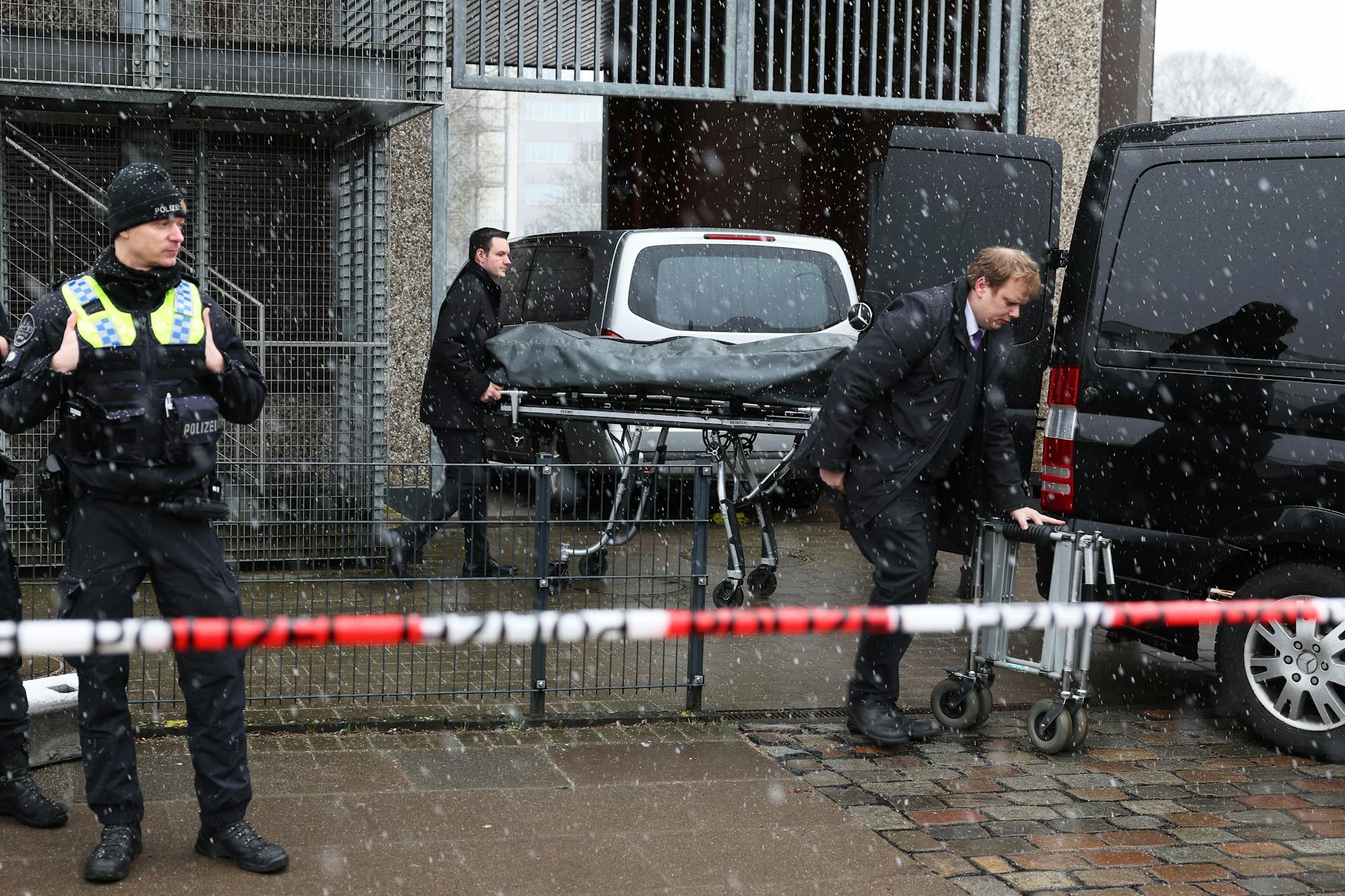 Bestatter bringen eine abgedeckte Bahre zu ihrem Fahrzeug am Gebäude der Zeugen Jehovas in Hamburg.