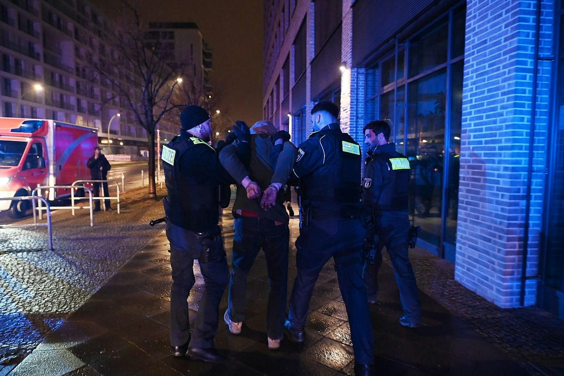 Hier führt die Polizei einen der mutmaßlichen Brandstifter in Handschellen ab.