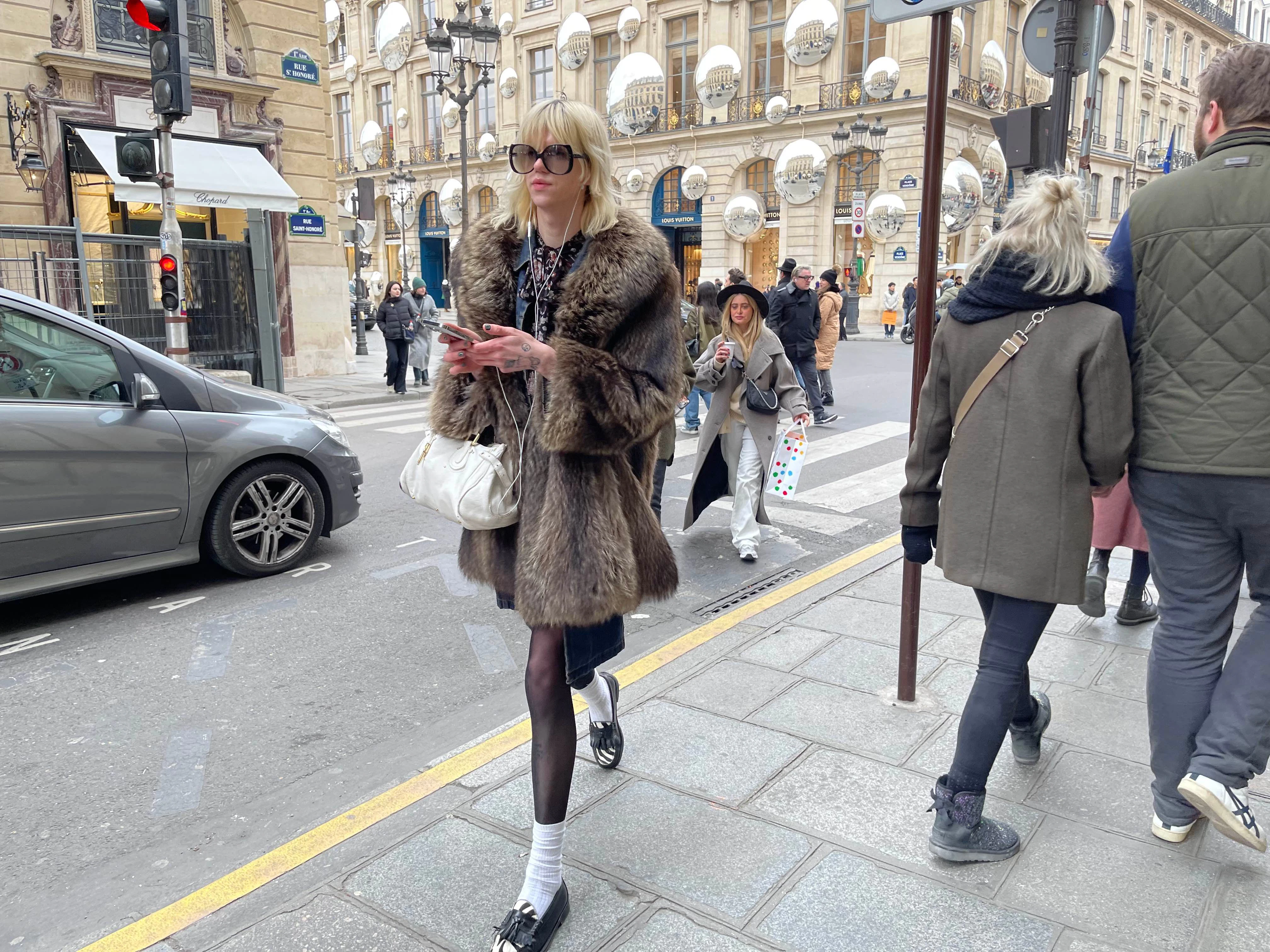 Pelz, ob echt oder unecht, sieht man viel in Paris. Hier mit blondem Pseudo-Vokuhila und weißen Söckchen. Hinten ist der Louis-Vuitton-Store am Place Vendôme zu sehen. An der Fassade sieht man eine temporäre Installation, die auf eine laufende Kollaboration mit der japanischen Künstlerin Yayoi Kusama verweist.
