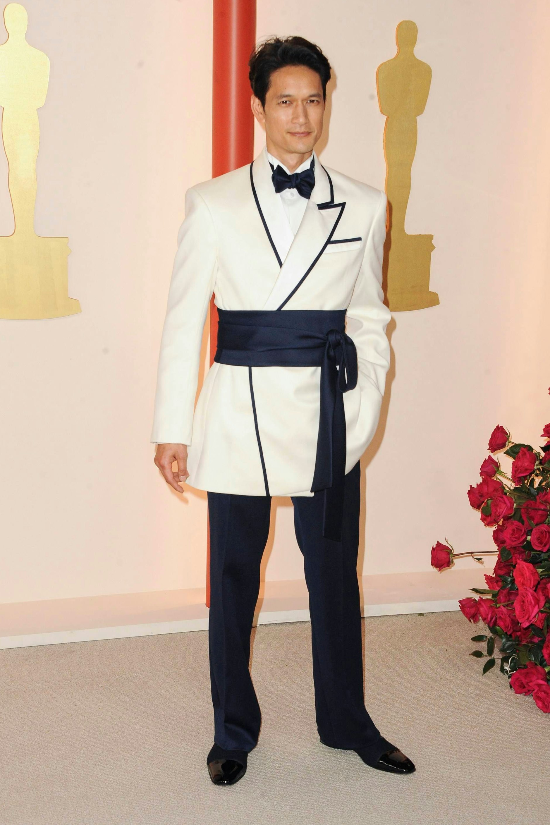 <strong>Flop:</strong>&nbsp;Komisches Teil, dieser Anzug. Auf der einen Seite mit einem Schal- und auf der anderen mit einem Reverskragen ausgestattet, beide schwarz gerahmt, dazu der nach außen getragene Kummerbund, der den Look brachial in zwei teilt. Einen Gefallen hat sich der Tänzer Harry Shum Jr. damit wirklich nicht getan. Außerdem: Das Hemd ist ein wenig zu weiß für die cremefarbene Jacke.