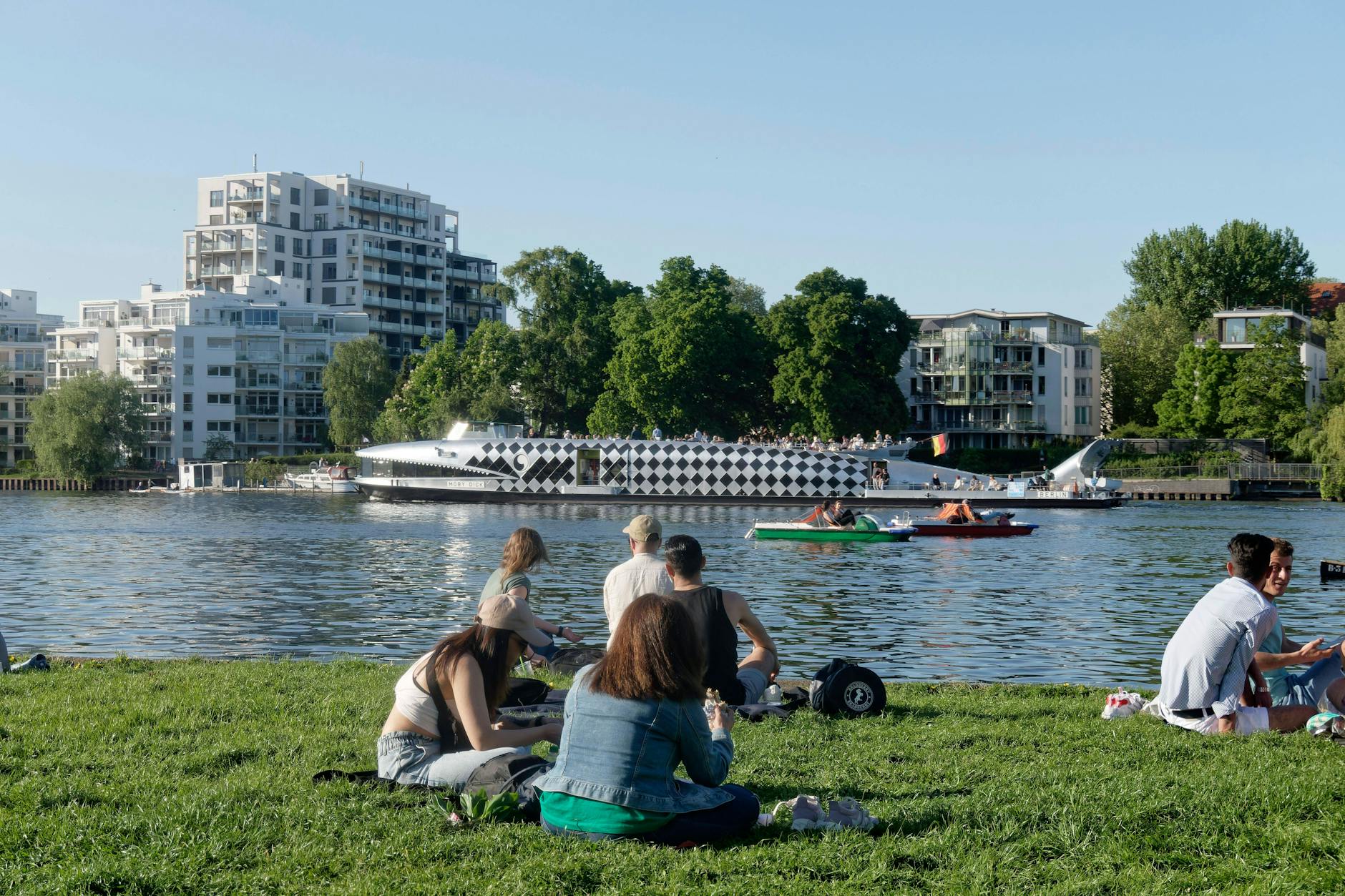 Junge Leute sitzen am Ufer der Spree in Berlin.