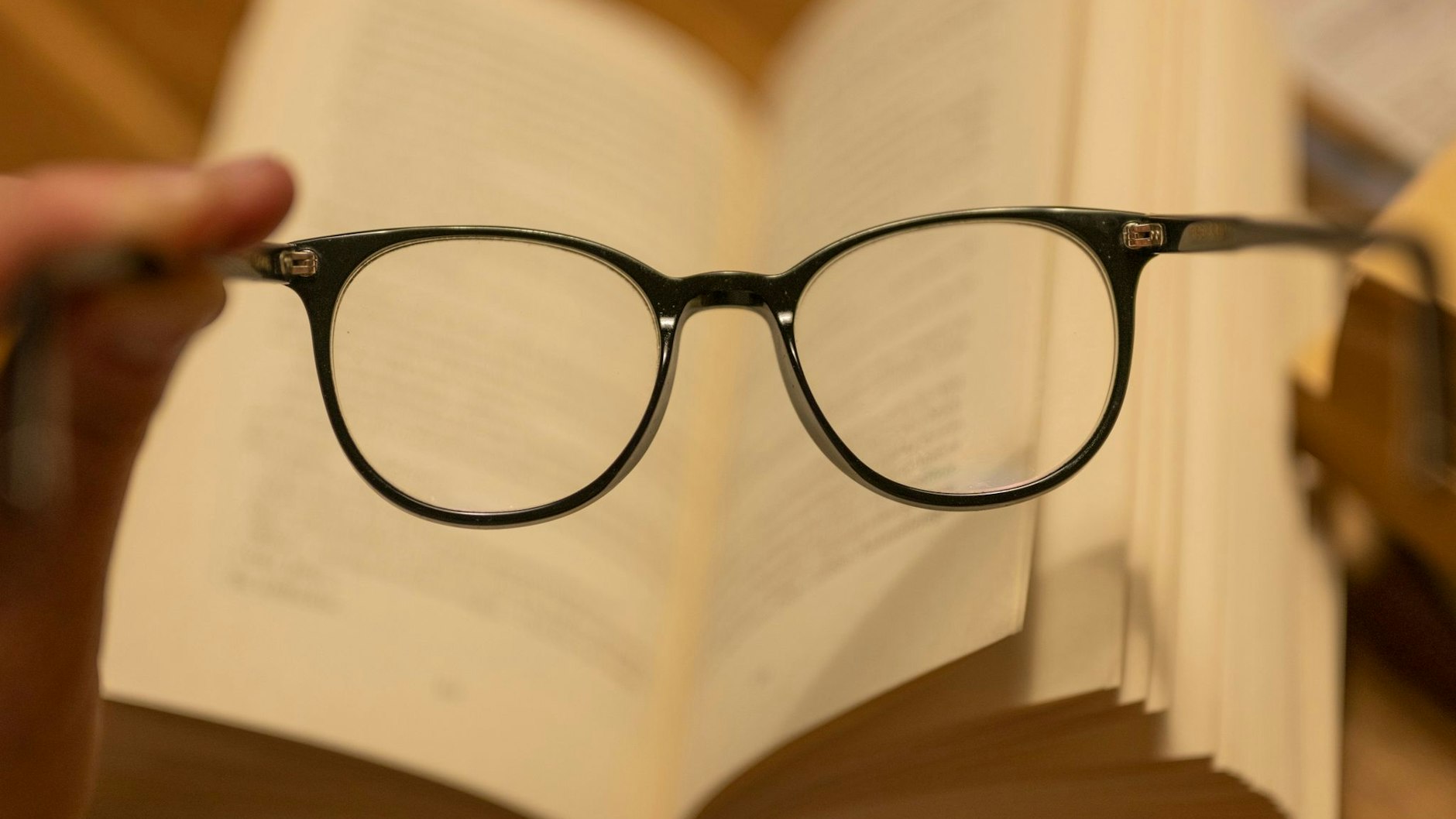 Ein Mann hält eine Lesebrille vor einem geöffneten Papierbuch. Die Abstände beim Arbeiten am Computer sind andere. 