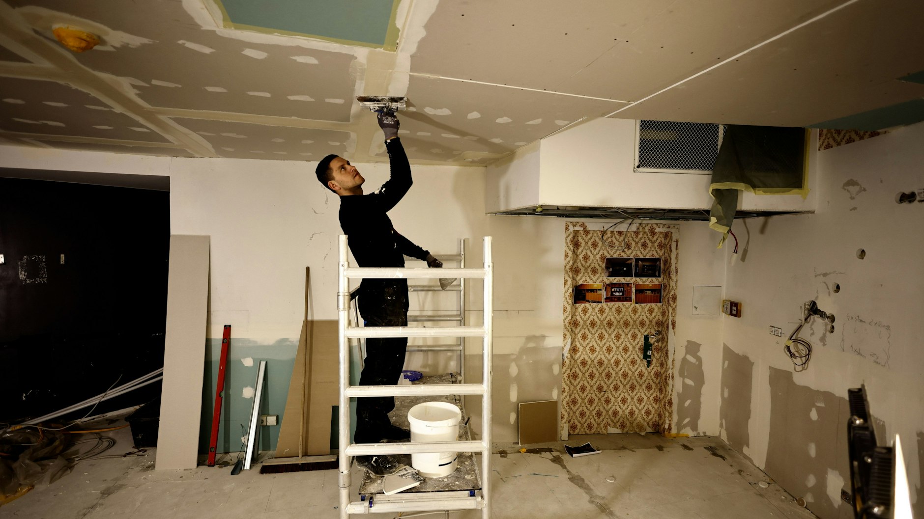 Ein Handwerker streicht die Decke in einem Teil einer originalgetreu nachgebauten DDR-Wohnung auf der Baustelle. Teile der Decke waren durch das Wasser heruntergekommen.&nbsp;
