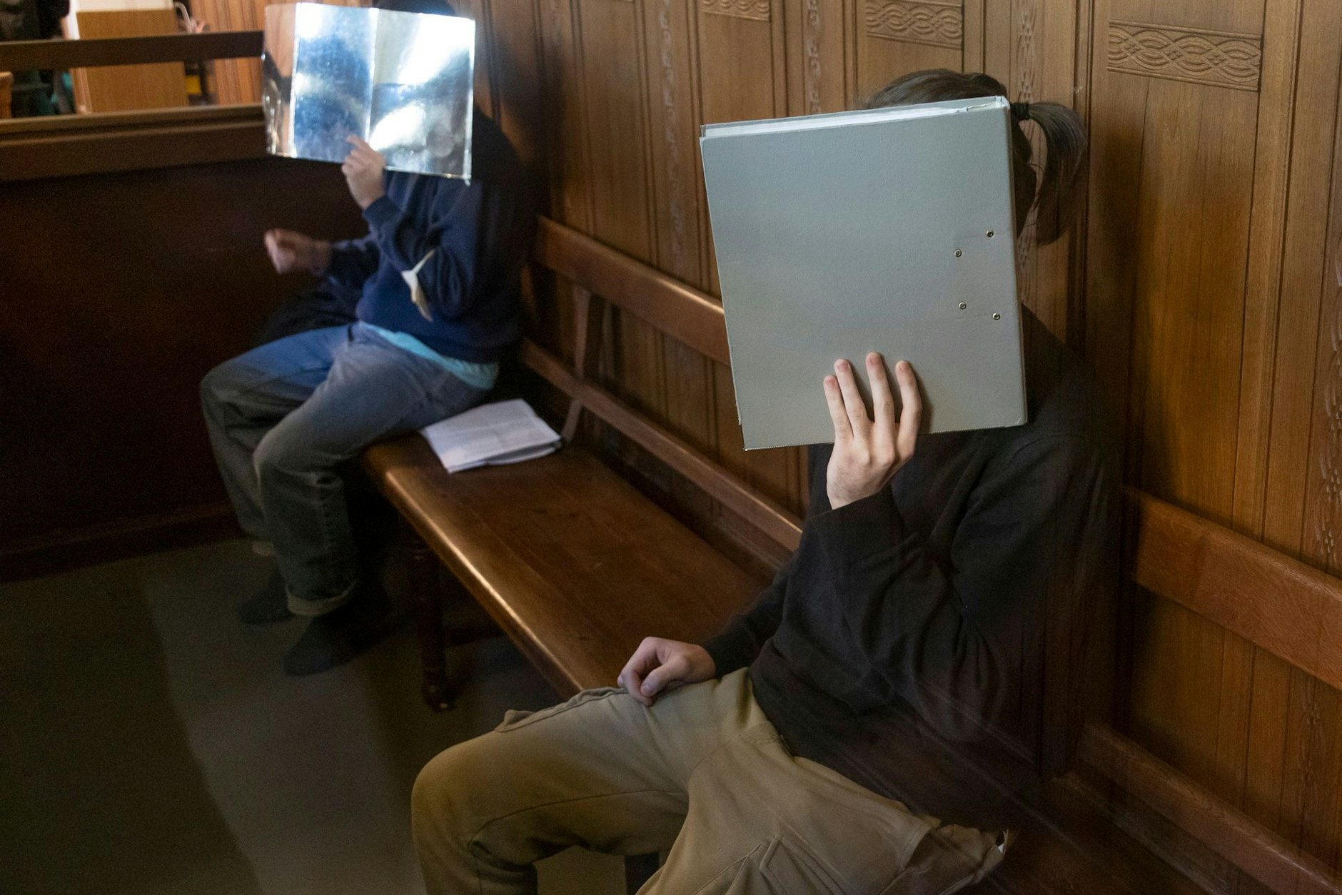 Zwei der Berliner Carjacker sitzen auf der Bank im Gerichtssaal und bedecken ihre Gesichter.