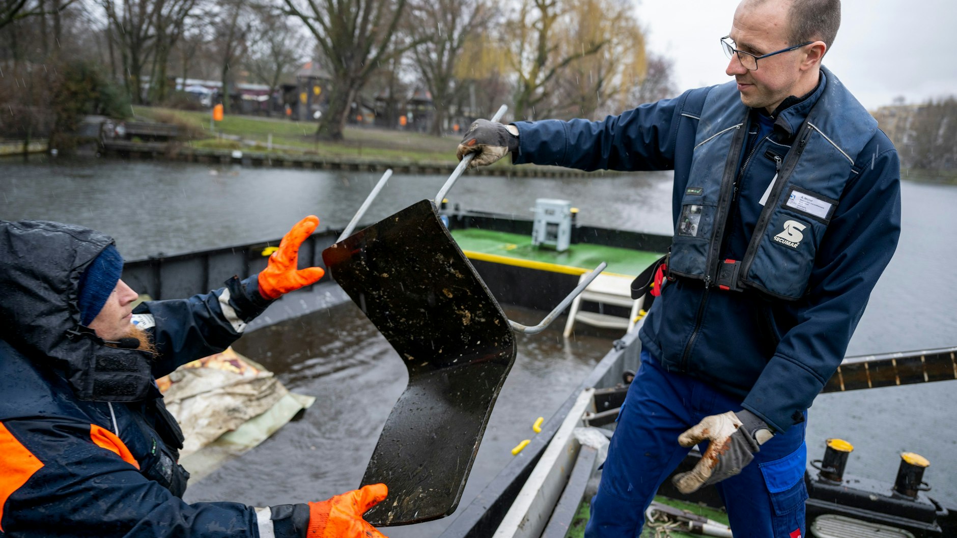 Andreas Müller (r) und Stephan Strauch, Mitarbeiter vom Wasser- und Schifffahrtsamt, verladen bei einer Schiffsfahrt zur Hindernisbergung im Landwehrkanal einen aus dem Wasser geholten Stuhl auf einen schwimmenden Container.&nbsp;&nbsp;