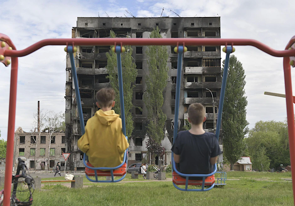 Zwei Kinder schaukeln vor einem durch russische Militärangriffe zerstörtes Wohngebäude in Kiew. Russland soll tausende ukrainische Kinder verschleppt haben.