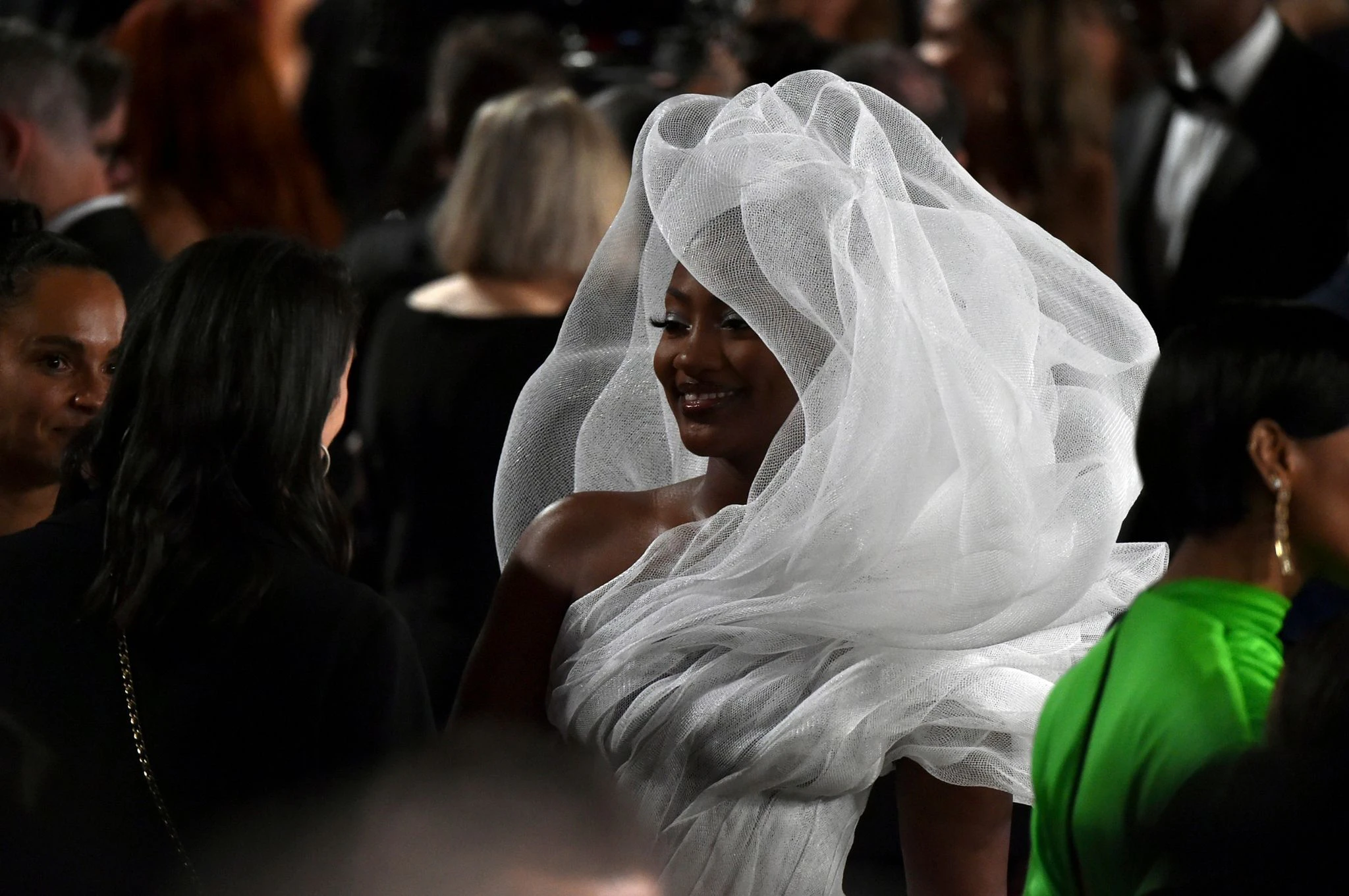 Sie fällt auf: Sängerin Tems kommt in einem aufregenden weißen Outfit zur Oscar-Verleihung. Weniger Glück hatten allerdings die Gäste, die im Saal hinter ihr saßen.  