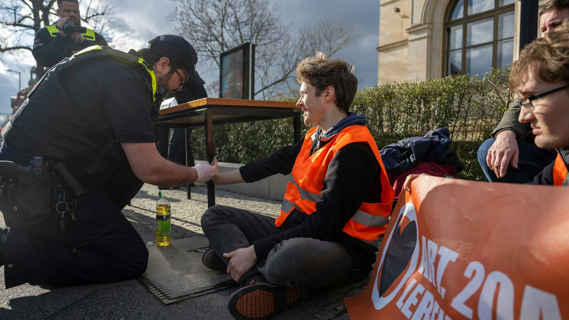 Klima-Kleber&nbsp; Henning Jeschke wird von einem Polizisten von dem Tisch gelöst. Für die Aktion schwänzte er seinen Prozess im Amtsgericht.&nbsp;