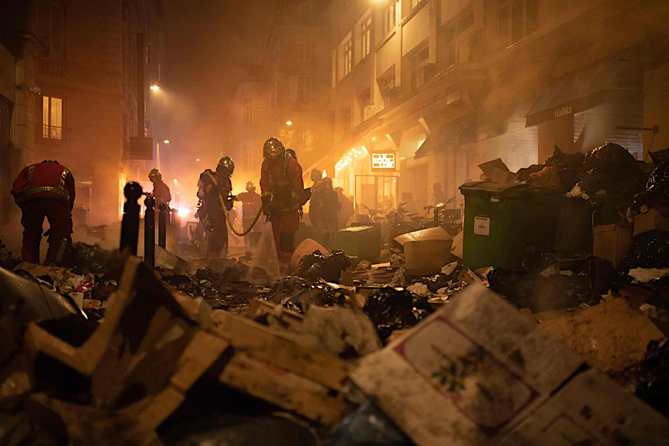 Feuerwehrleute kontrollieren Müll nach dem Löschen eines Feuers während einer Demonstration.