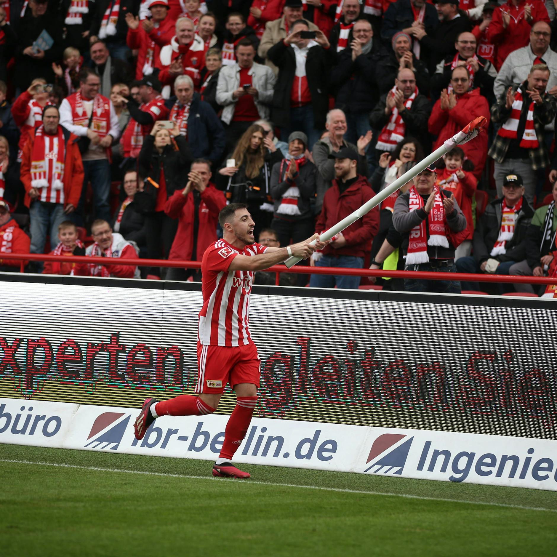 Josip Juranovic feiert den Sieg des 1. FC Union auf seine Weise, indem er eine Eckfahne zu einem Winkinstrument umfunktioniert.