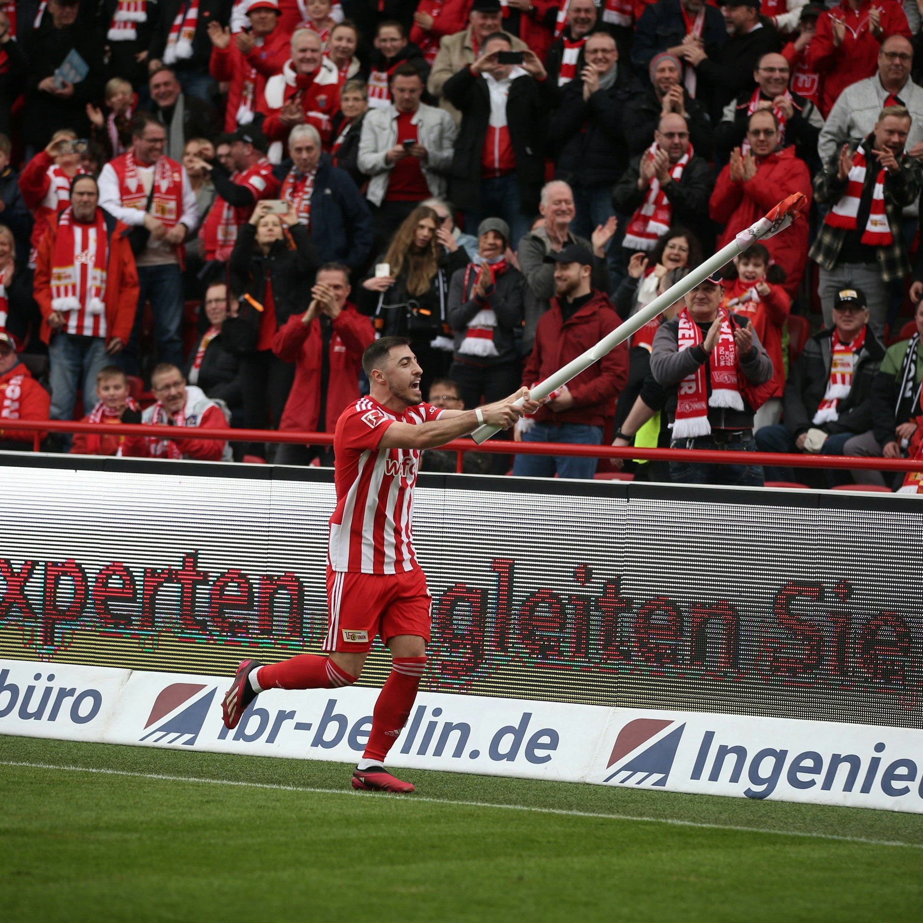 Josip Juranovic feiert den Sieg des 1. FC Union auf seine Weise, indem er eine Eckfahne zu einem Winkinstrument umfunktioniert.