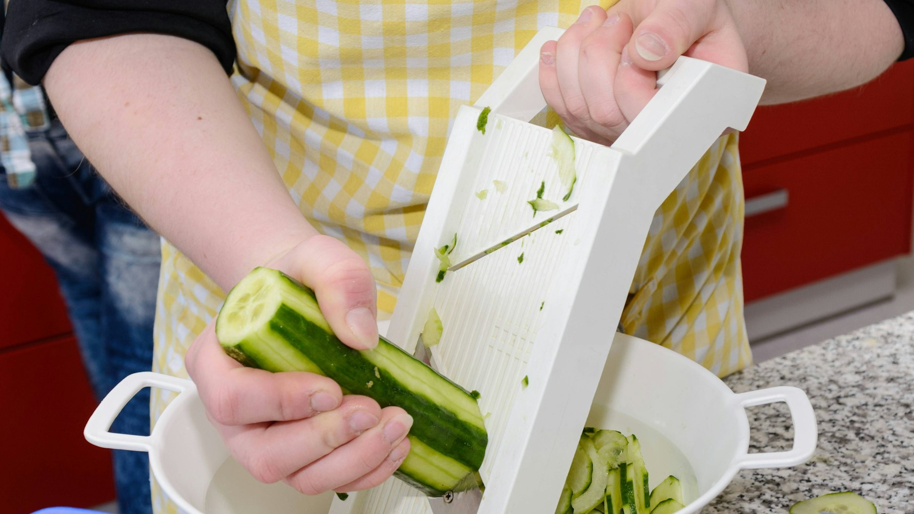 Für den Gurkensalat wird die Gurke mit dem Hobel in feine Scheiben geschnitten.