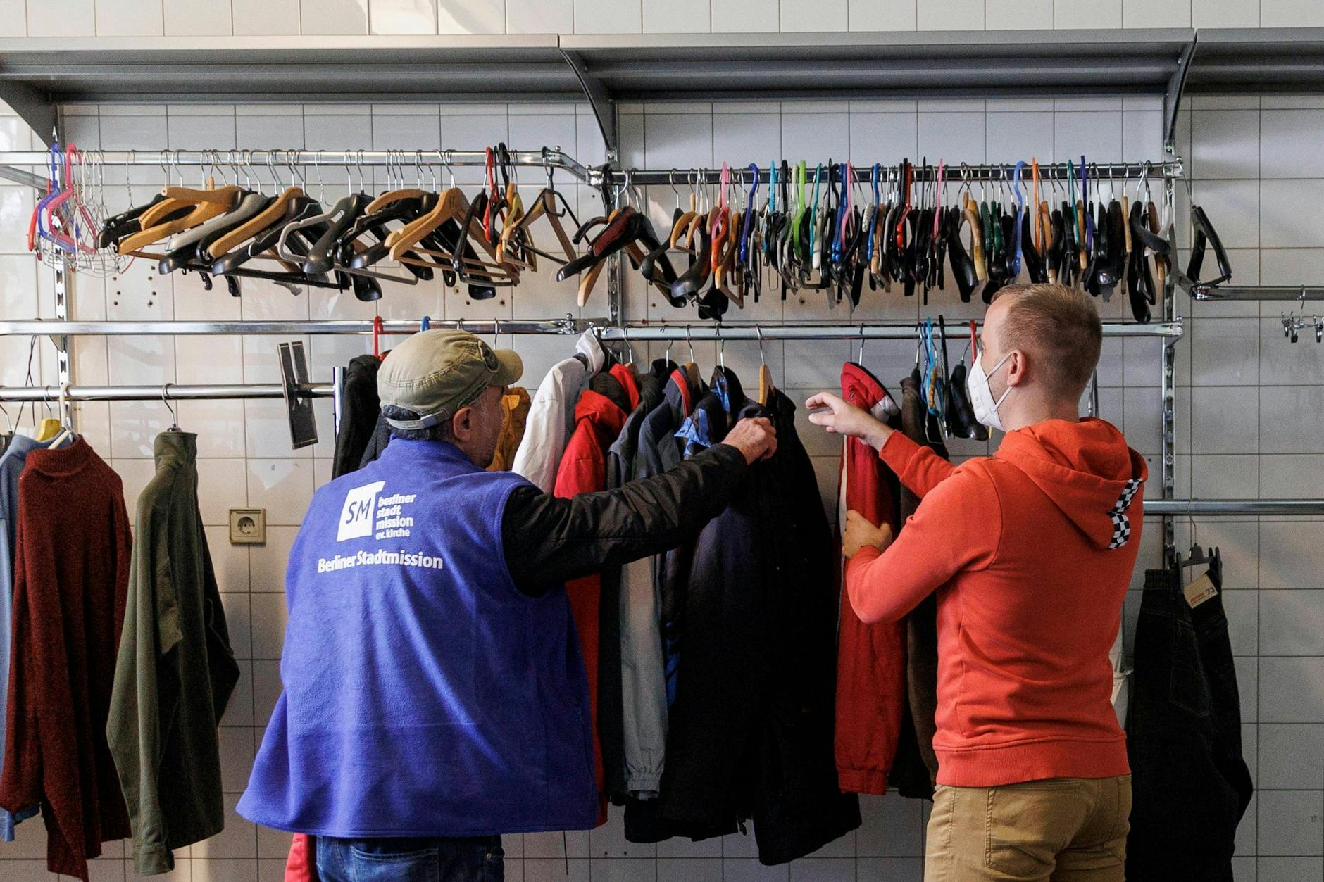 Mitarbeiter der Berliner Stadtmission stehen vor einer Kleiderstange in der Kleiderkammer. 