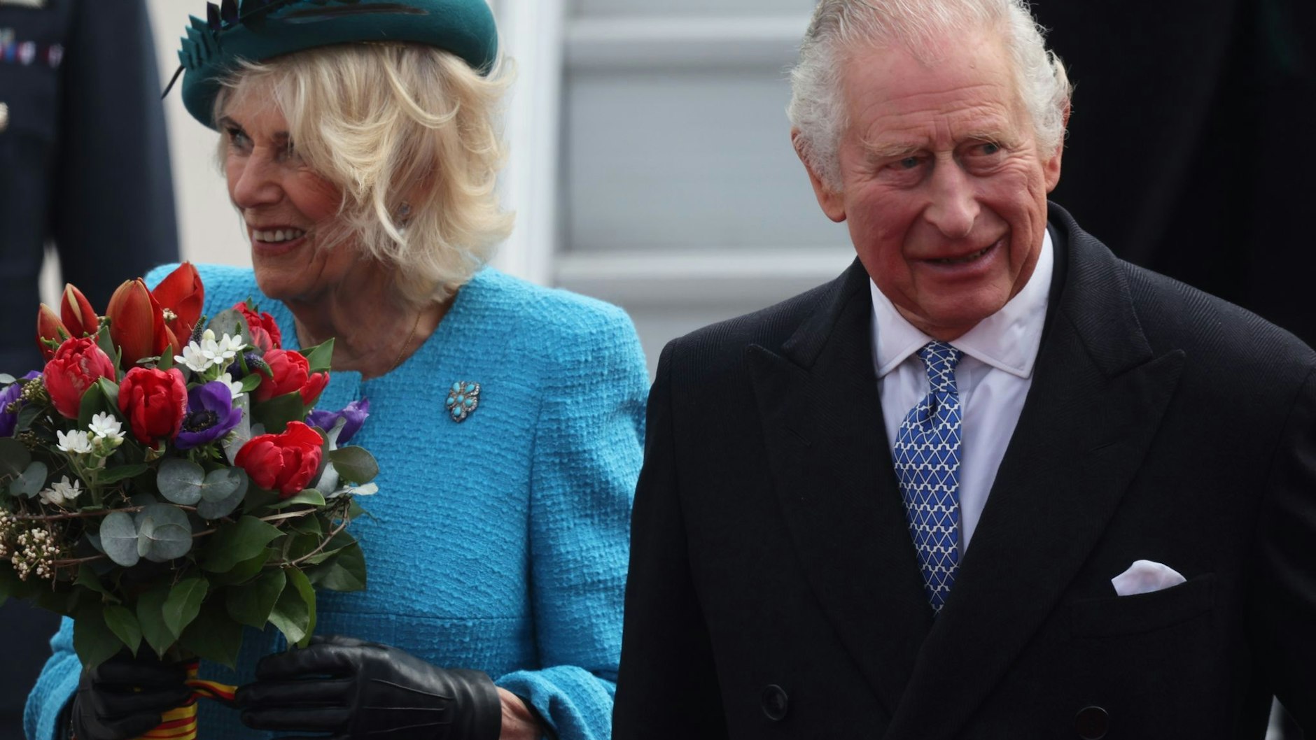 Ein Frühlingsblumenstraß für Camilla: Sie und König Charles III. werden schon am Flughafen BER herzlich begrüßt.