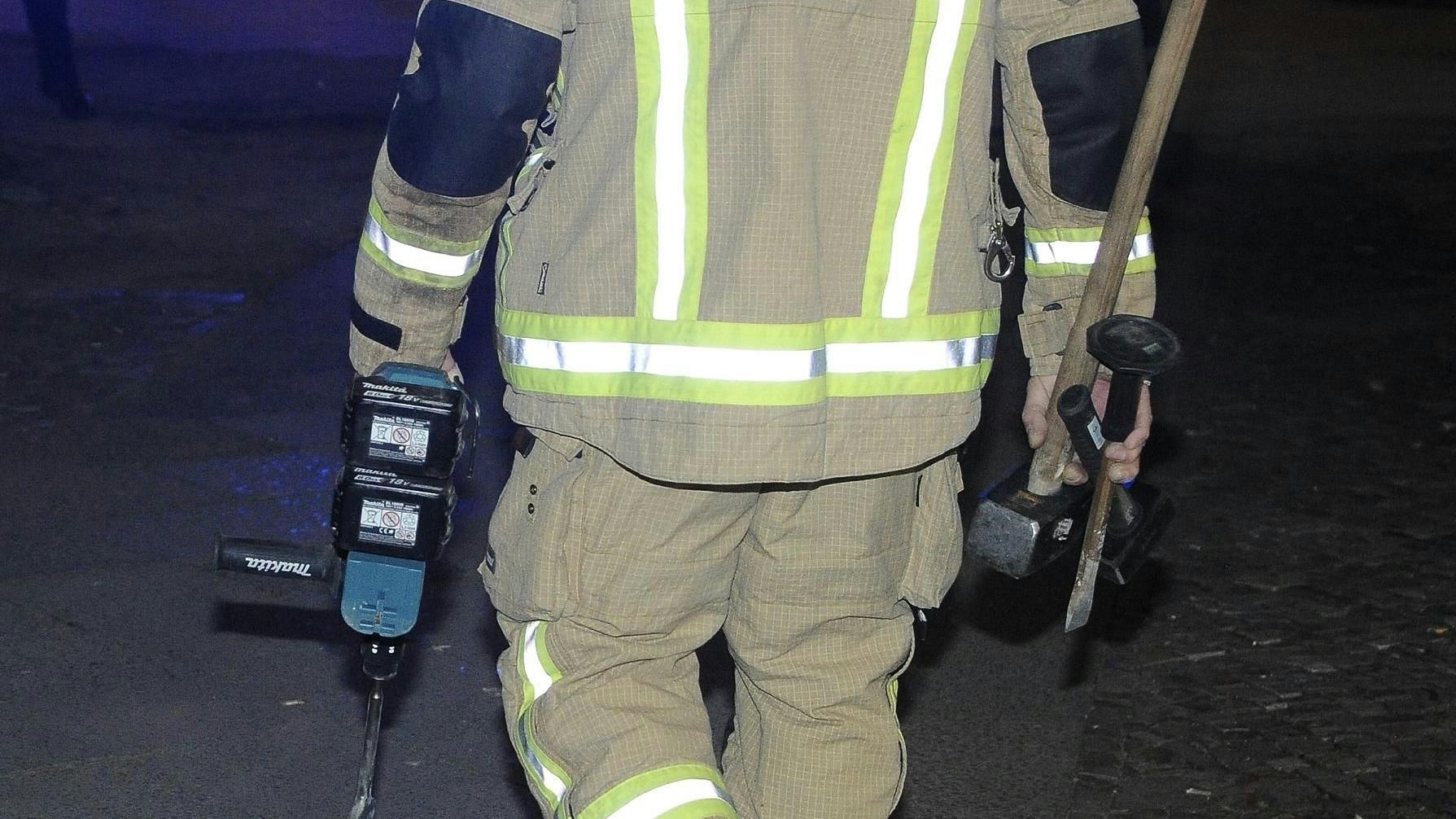 Ein Feuerwehrmann mit den Gerätschaften, mit denen der Schornstein aus einer Wohnung heraus aufgestemmt wurde, um den darin feststeckenden Mann zu befreien.