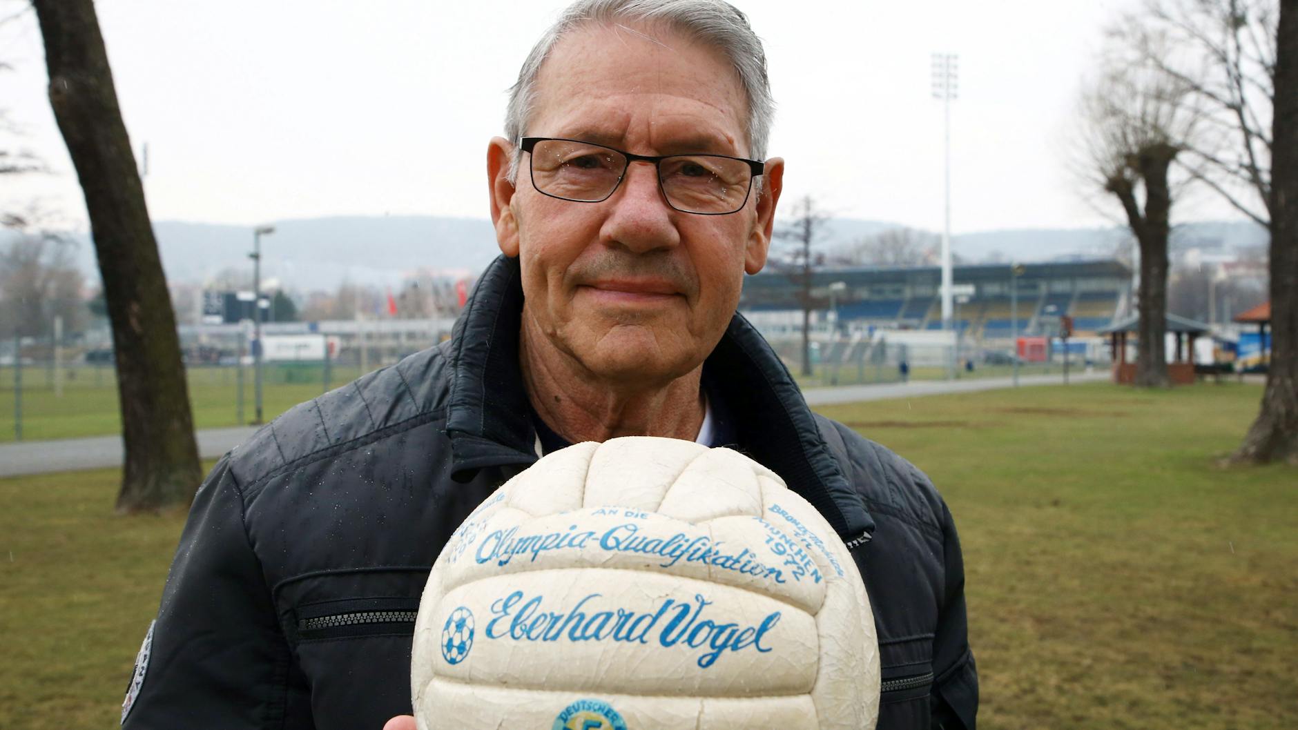 Ein Foto aus dem März 2018: Eberhard Vogel steht mit dem Originalball der Olympiaqualifikation von 1972 auf dem Gelände des Ernst-Abbe-Sportplatzes in Jena.