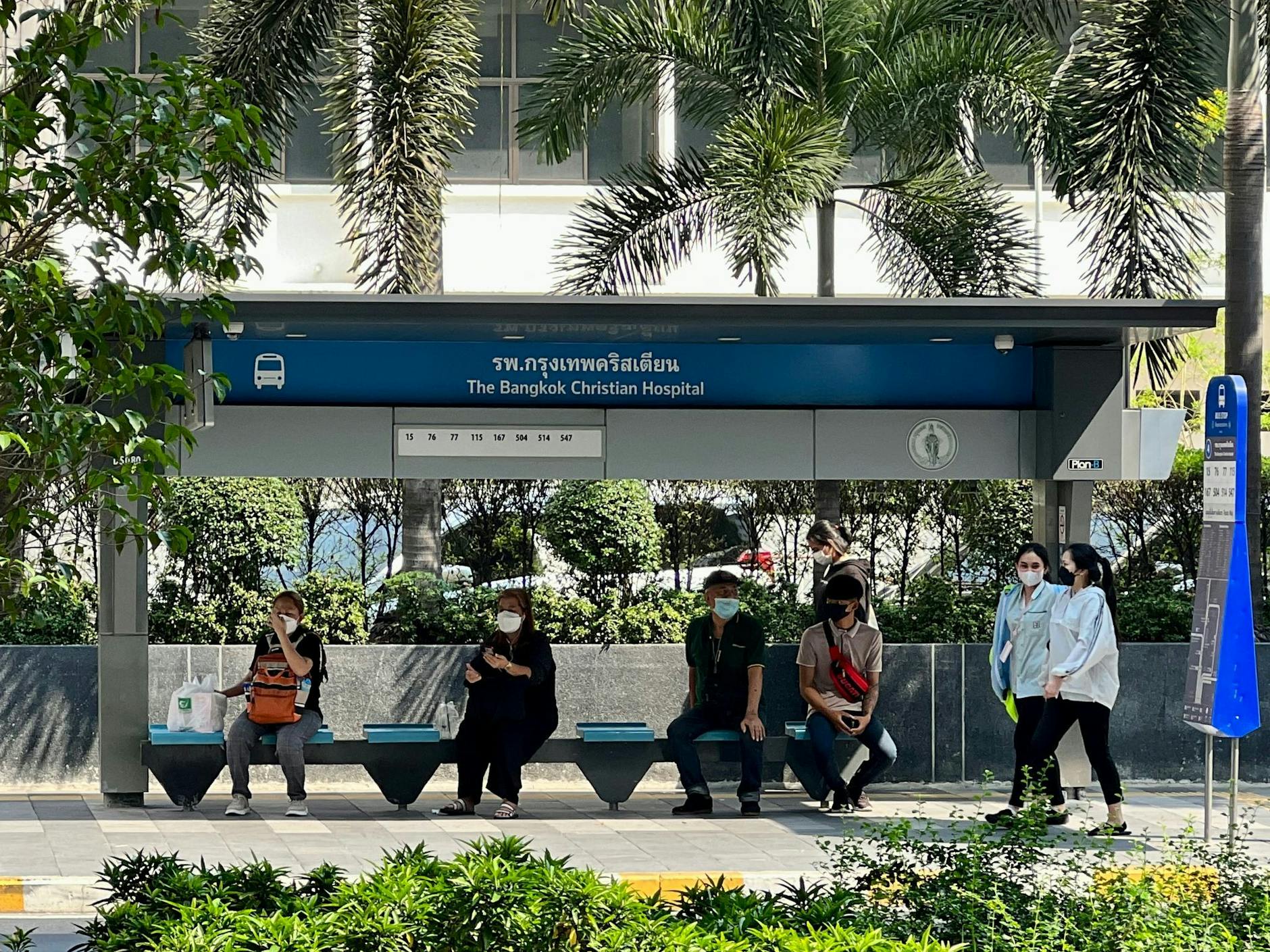 Menschen suchen im Schatten einer Bushaltestelle in Bangkok Schutz vor der Sonne.