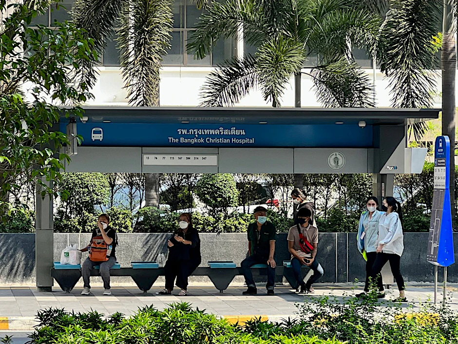 Menschen suchen im Schatten einer Bushaltestelle in Bangkok Schutz vor der Sonne.  