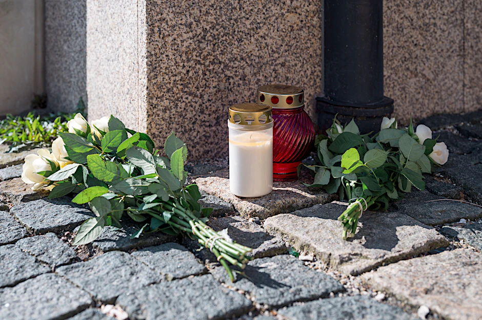Wunsiedel: An der Straßenecke zur Zufahrtsstraße zum Kinder- und Jugendhilfezentrum, in dem eine Zehnjährige tot aufgefunden wurde, liegen Blumen und Grablichter auf dem Gehweg.