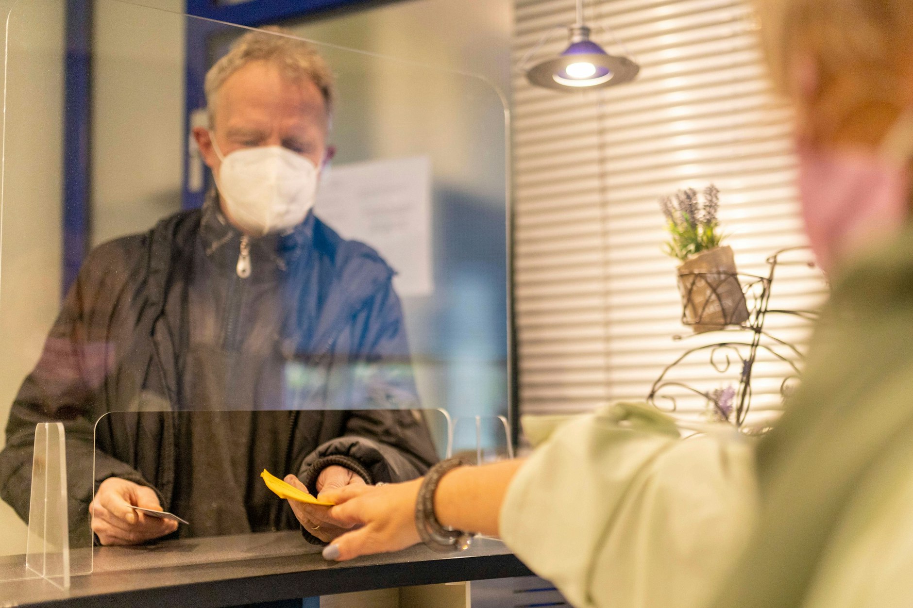Ein Mann mit Mund-Nasen-Schutz nimmt in einer Arztpraxis seinen Impfpass entgegen.